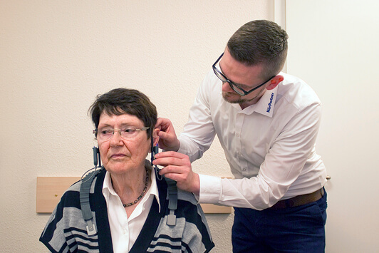 Ein Hörakustiker passt einer älteren Frau ein modernes Hörgerät im Fachgeschäft an.